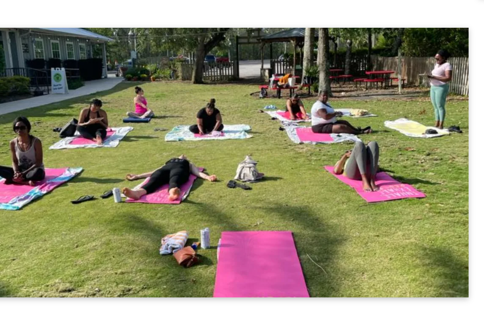 Four people sitting on colorful yoga mats on a tiled floor in a studio space, smiling at the camera.