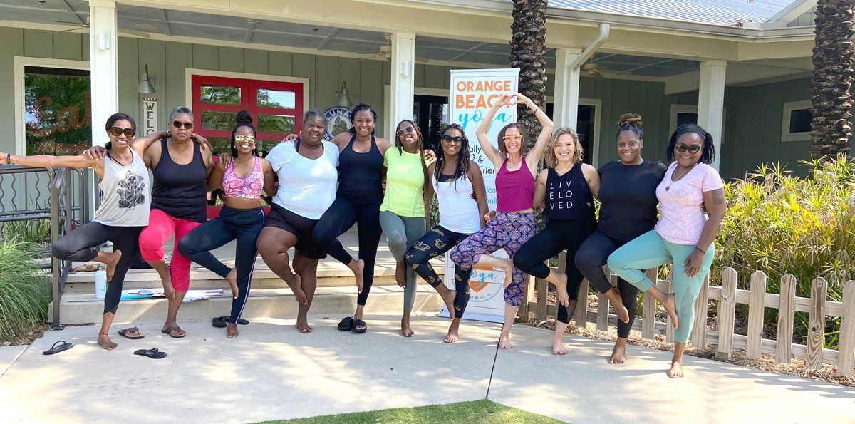 A group of people standing in a row in front of a house, balancing on one leg in a yoga pose outdoors.