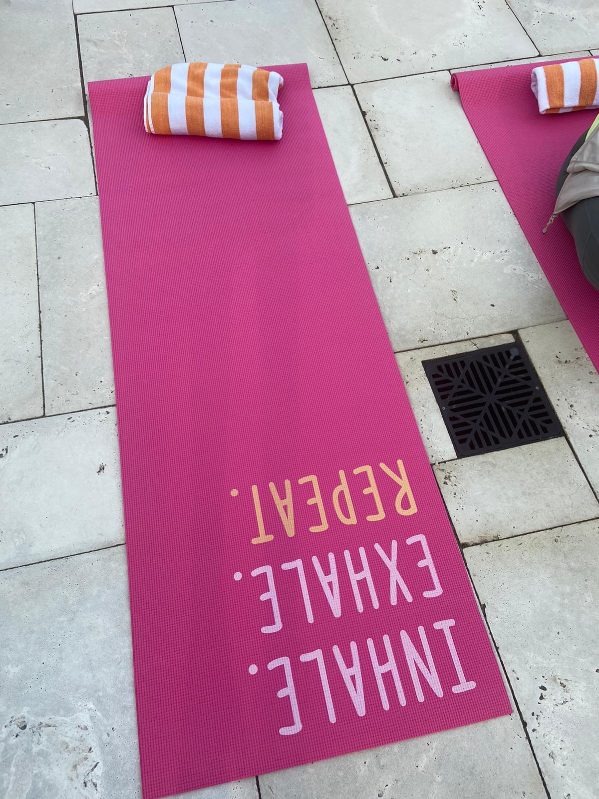 Two pink yoga mats with orange striped towels rest on a stone patio, one with the text 