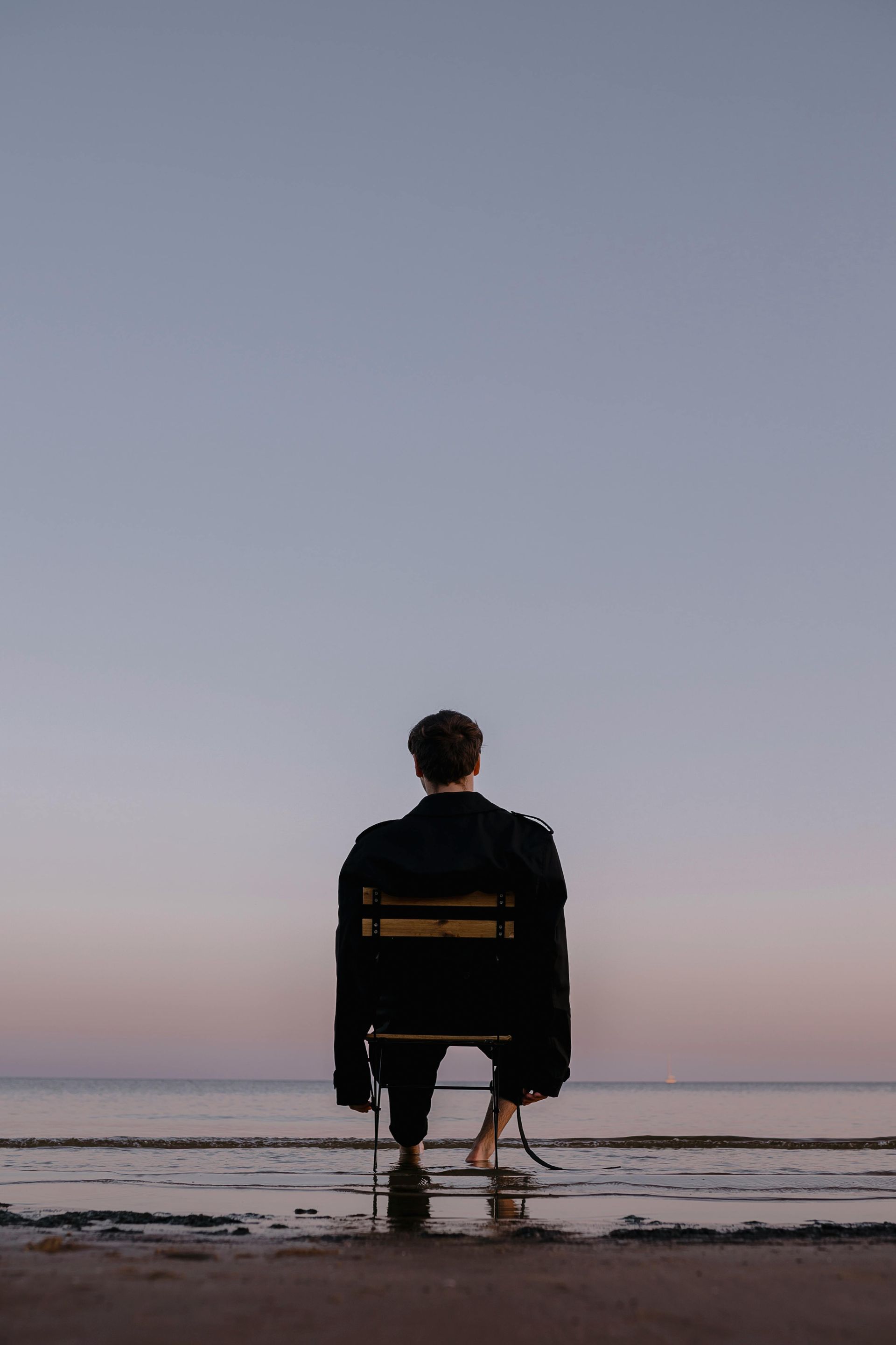 A man is sitting in a chair on the beach looking at the ocean.
