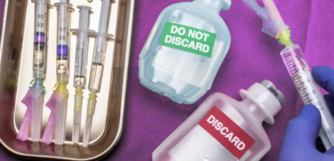 A person is holding a syringe next to a bottle that says do not discard.