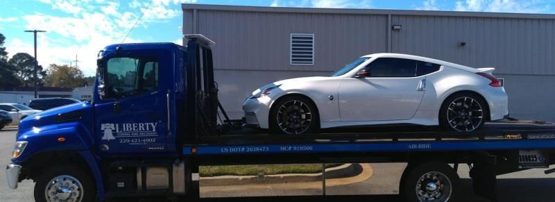 A white sports car on a blue tow truck in front of a gray building.