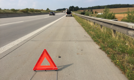 Red warning triangle on the side of a highway with a vehicle and passing cars.