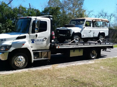 White Land Rover being towed on a flatbed tow truck by Liberty Towing. Sunny day.