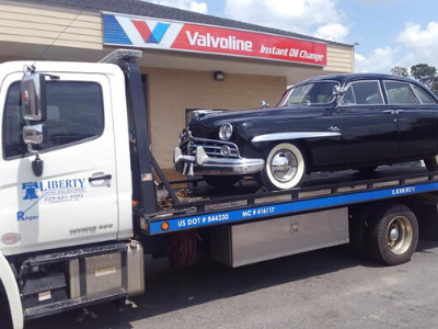 Black classic car on a tow truck in front of a Valvoline shop.