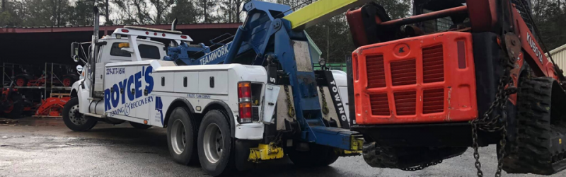 A tow truck lifting a red skid steer loader, likely for transport.