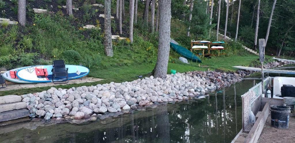 A kayak sits on the shore of a lake. Trees and a picnic table are in the background.