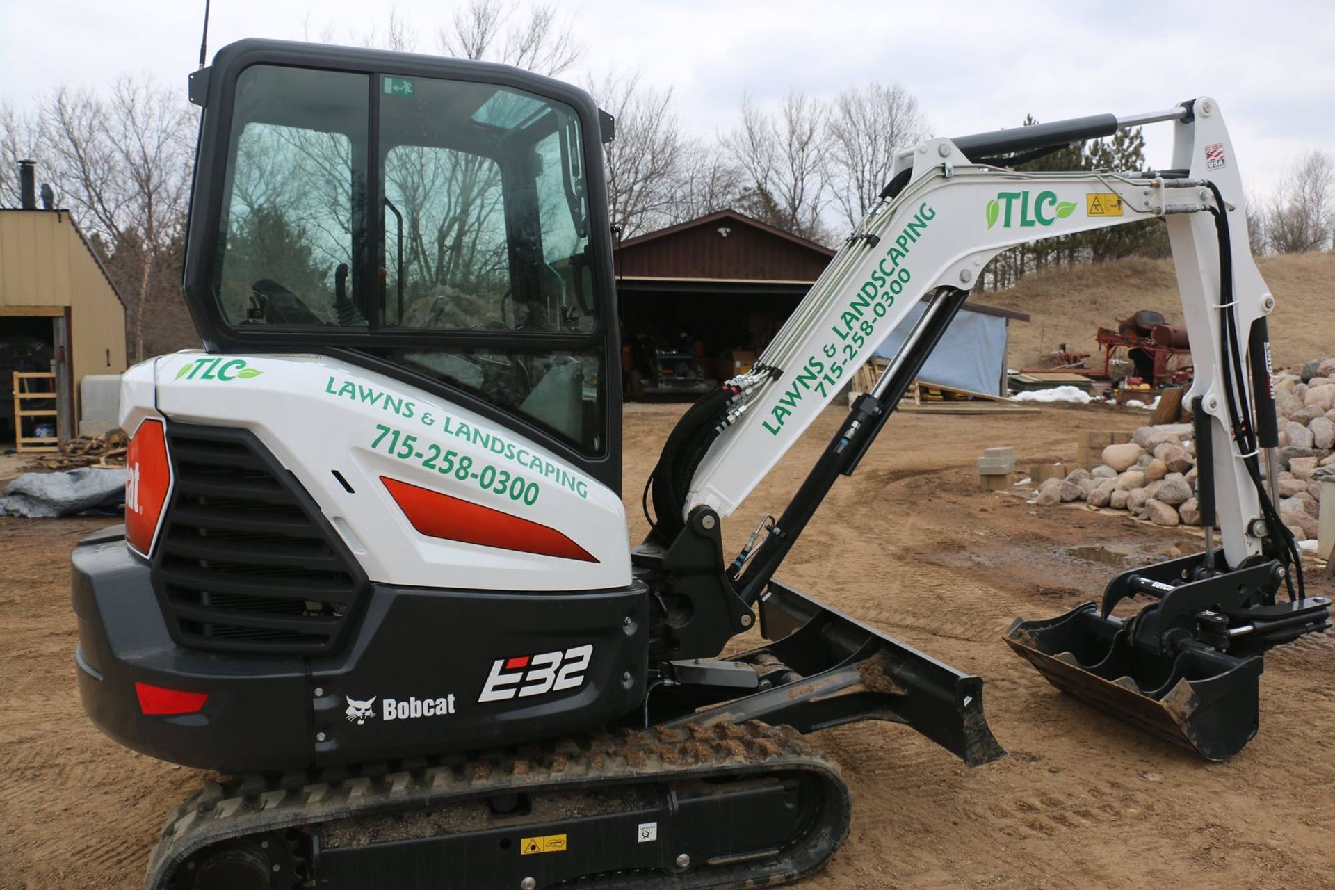 Bobcat E32 mini excavator with TLC Lawns & Landscaping logo. Outdoors, daylight.