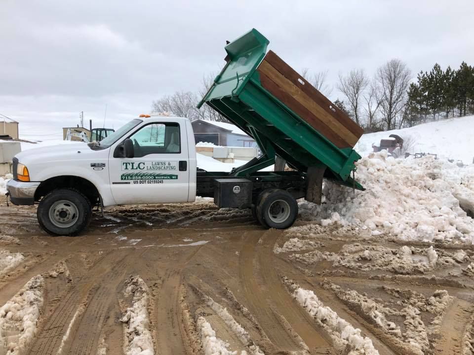 White dump truck dumping snow on a muddy road, overcast sky.