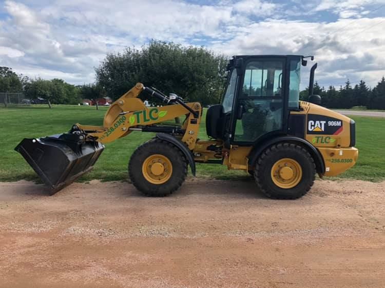 Yellow CAT 906M wheel loader on gravel with bucket in front.