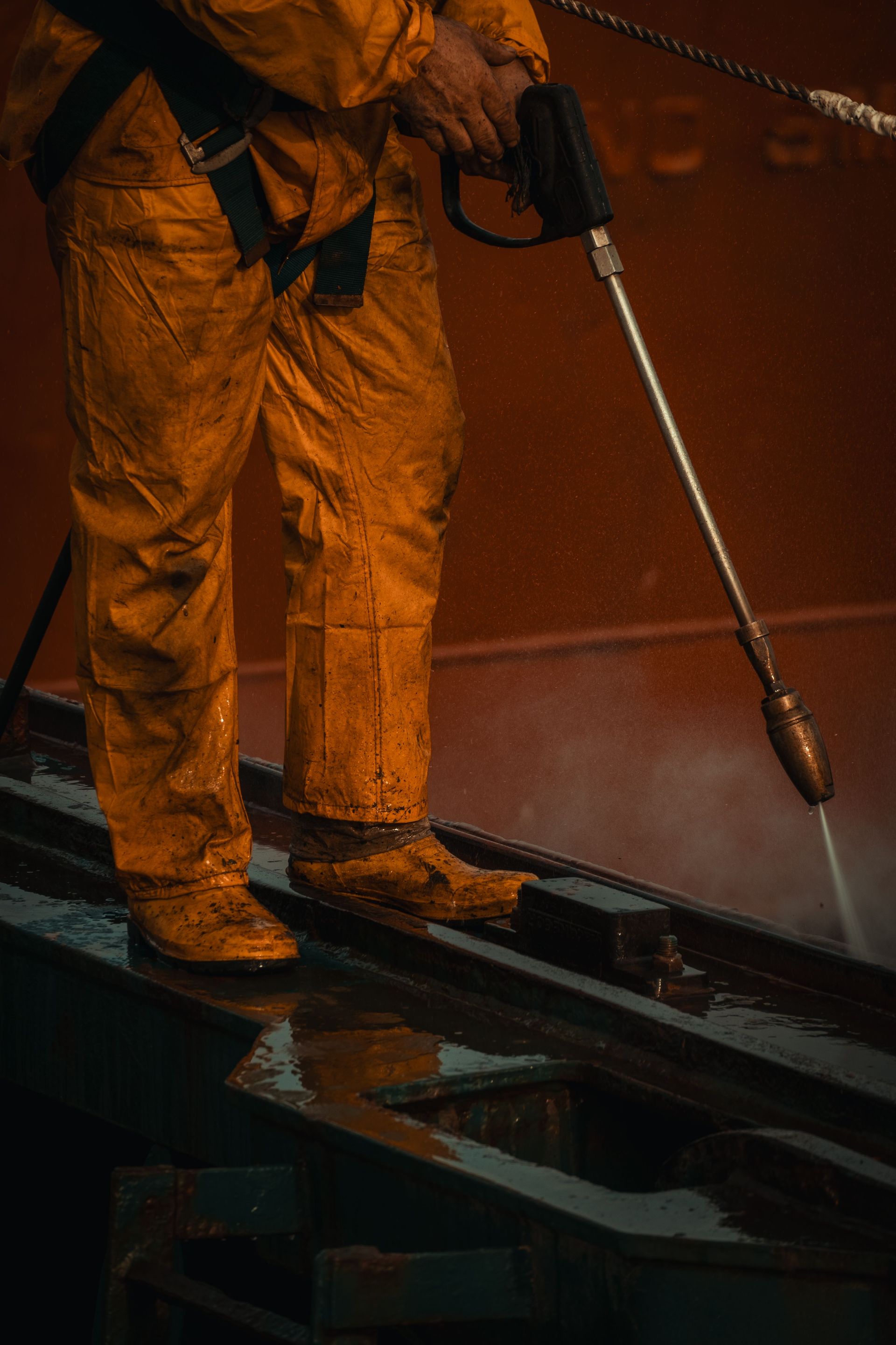 Worker in orange protective gear spraying water on a wet industrial surface at night