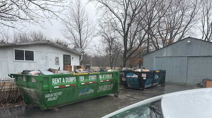 A green 15 yard dumpster is sitting in front of a black 15 yard dumpster maize