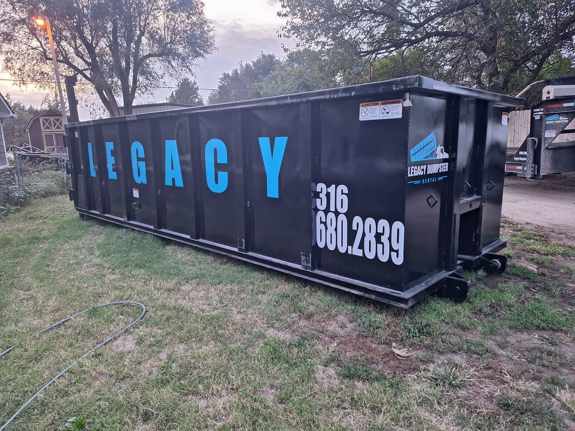 A large black 40 yard dumpster is sitting on top of a lush green field in Wichita, KS.