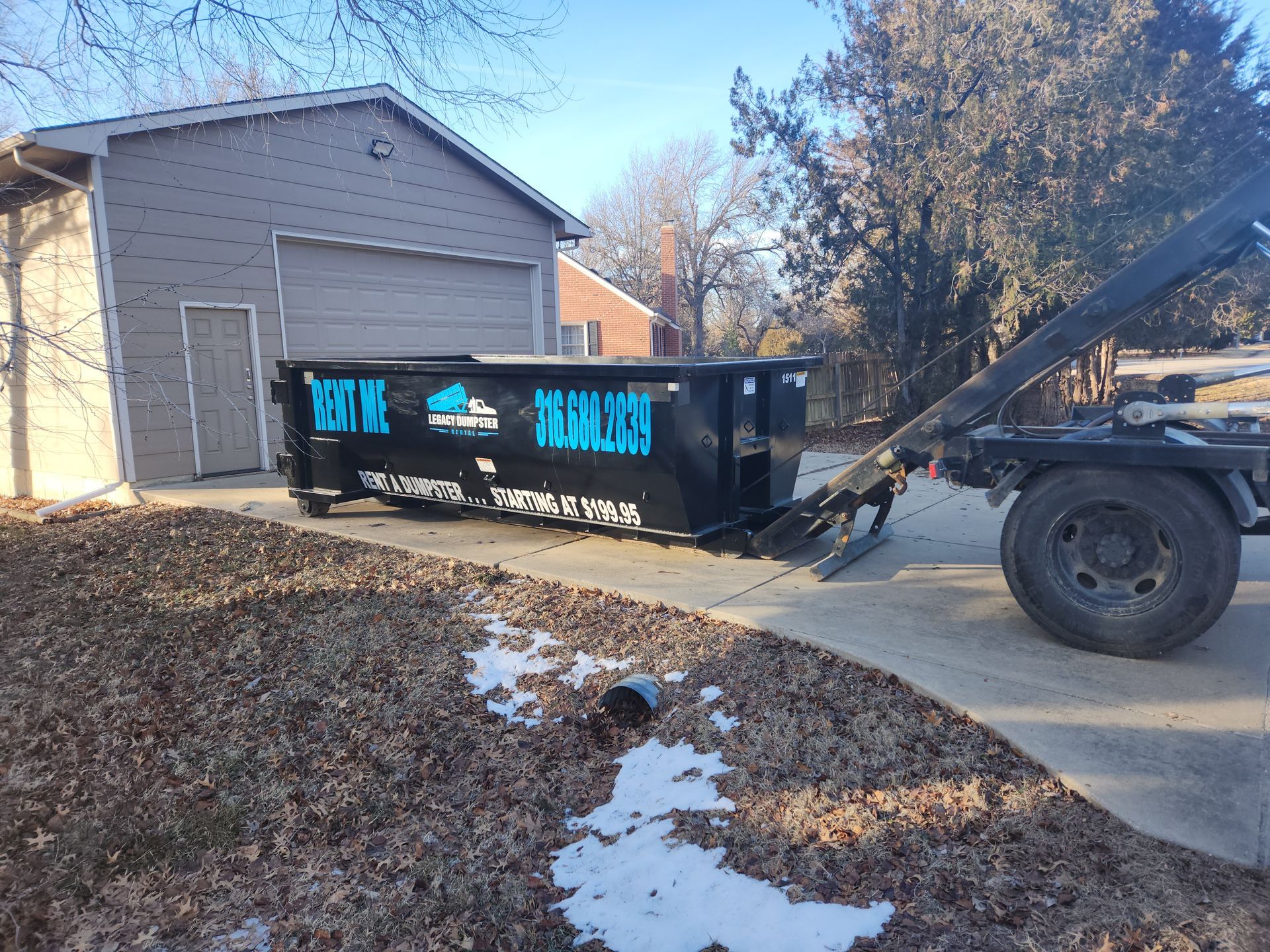 A dumpster is sitting in a driveway next to a garage.