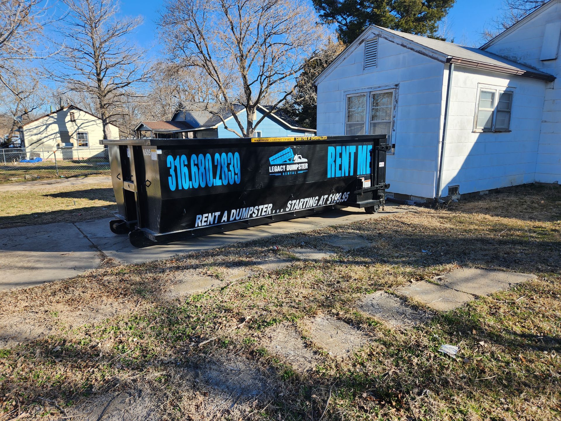 A 15 ayrd dumpster is parked in a driveway in front of a garage in Wichita, KS