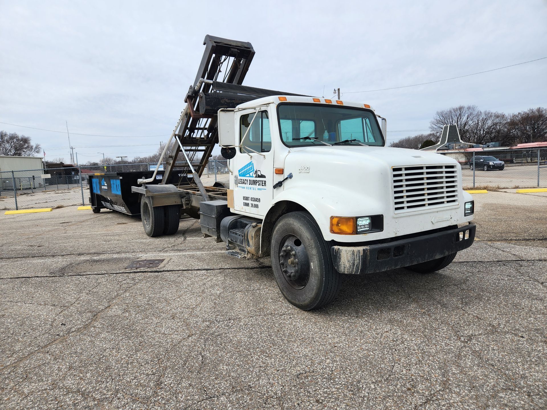 A dump truck with a forklift attached to it is parked in a parking lot.