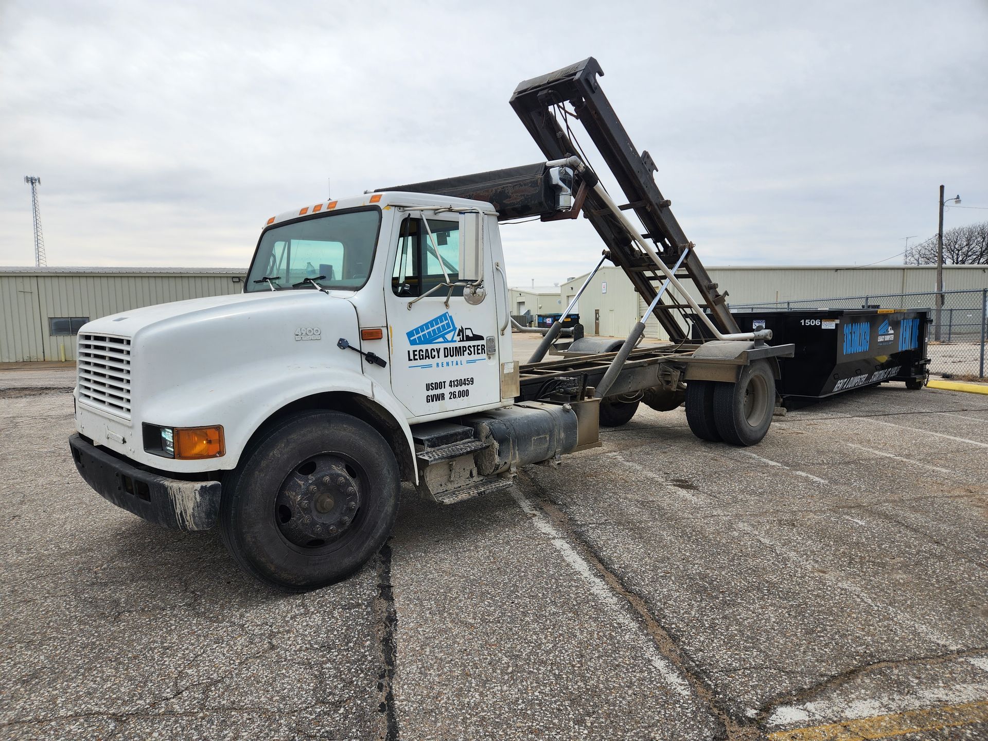 A dump truck is parked in a parking lot next to a dumpster.