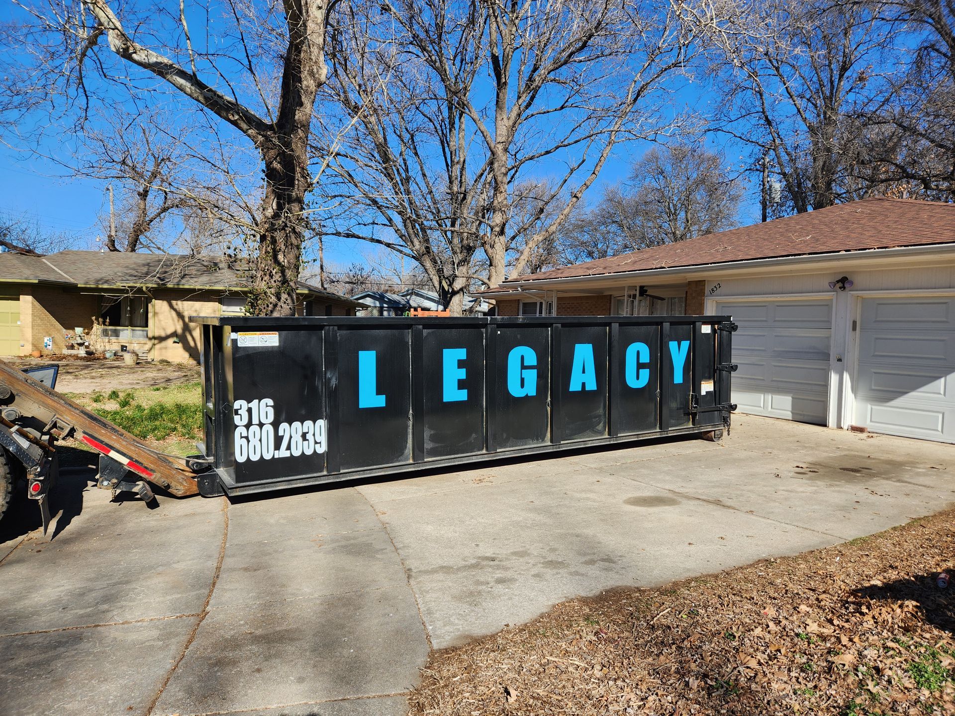 A dumpster with the word legacy on it is parked in front of a house.