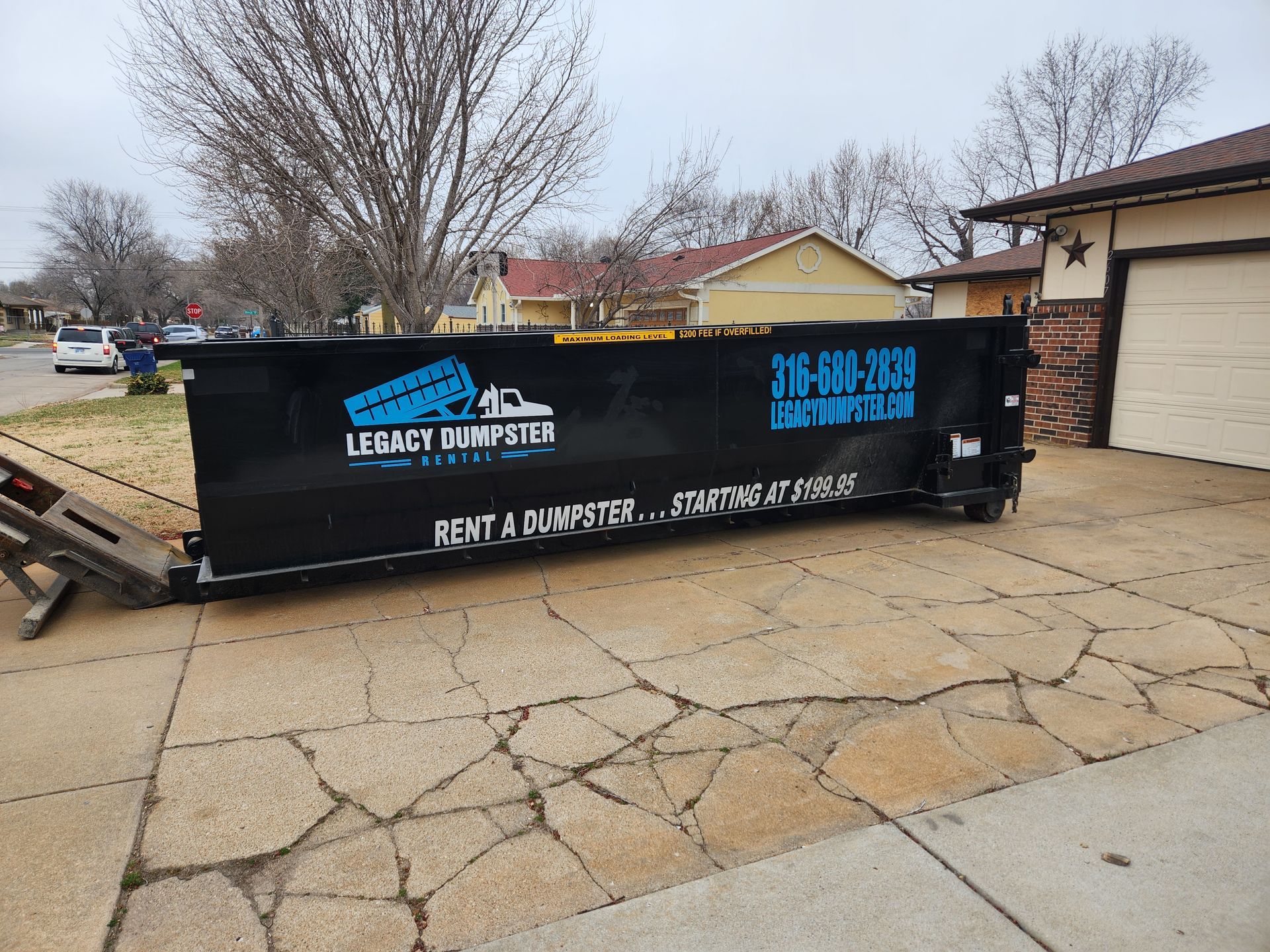 A black dumpster is parked on the side of the road in front of a house.