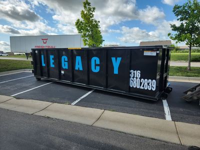 A large black 30 yard dumpster is being dropped off from a trailer onto a driveway.