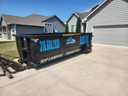 A 15 ayrd dumpster is parked in a driveway in front of a garage in Wichita, KS