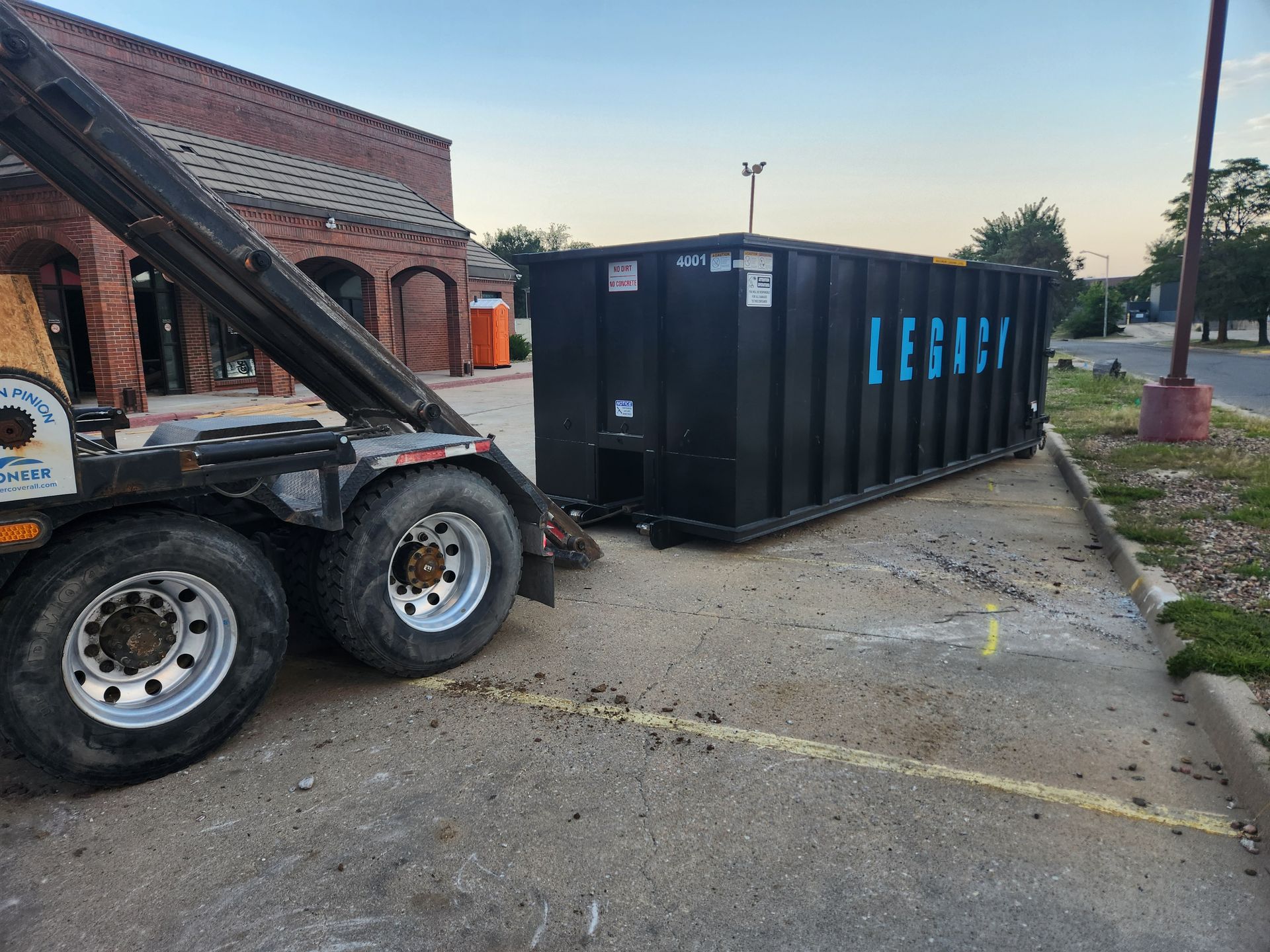 A dumpster is being loaded onto a truck in a parking lot.