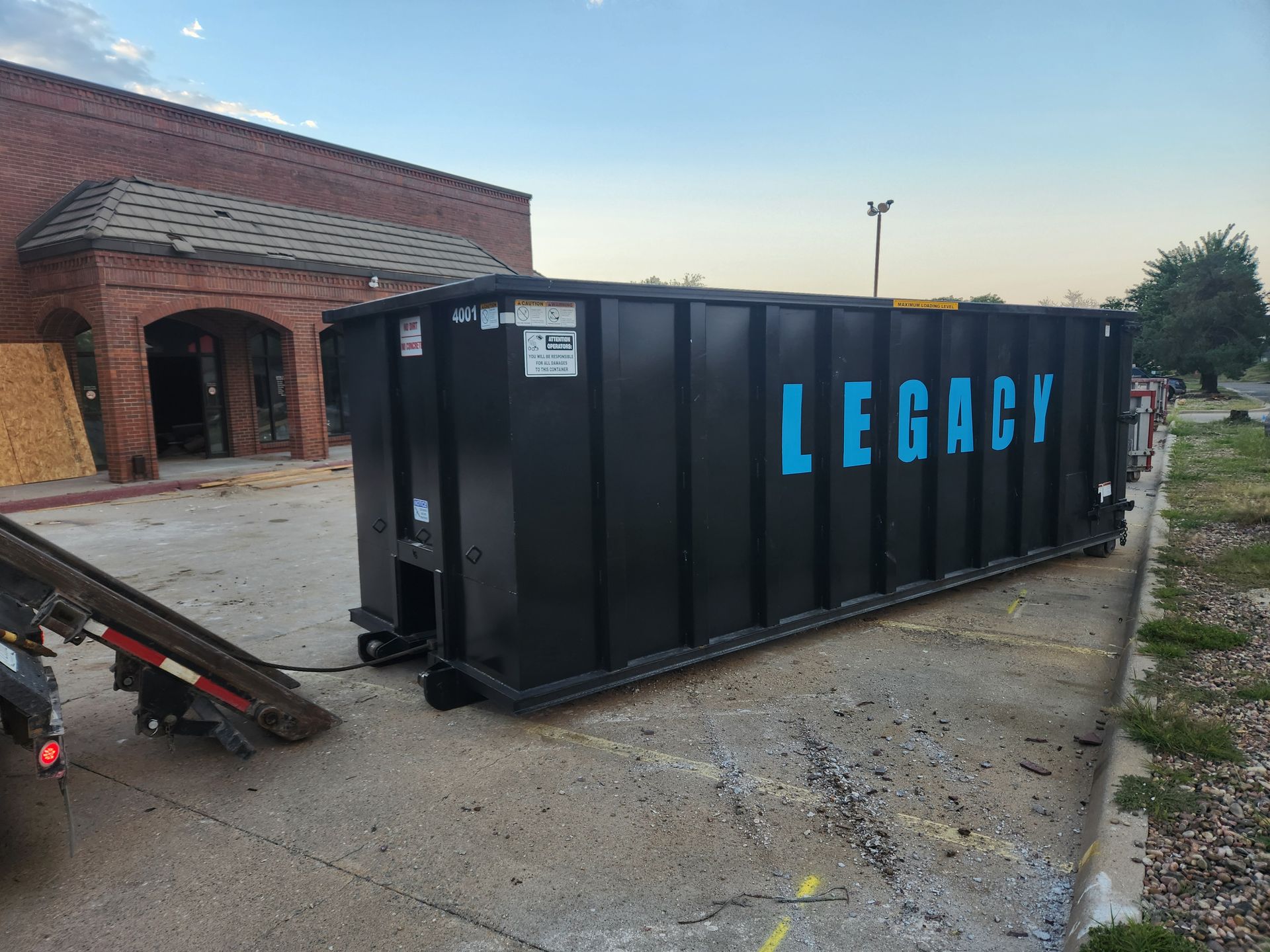 A large black dumpster is parked in front of a brick building.