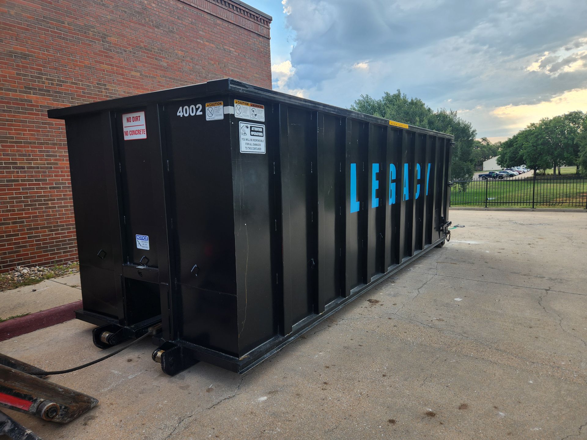 A large black dumpster is parked in front of a brick building.