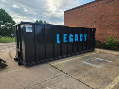 A large black 40 yard dumpster is sitting on top of a lush green field in Wichita, KS.