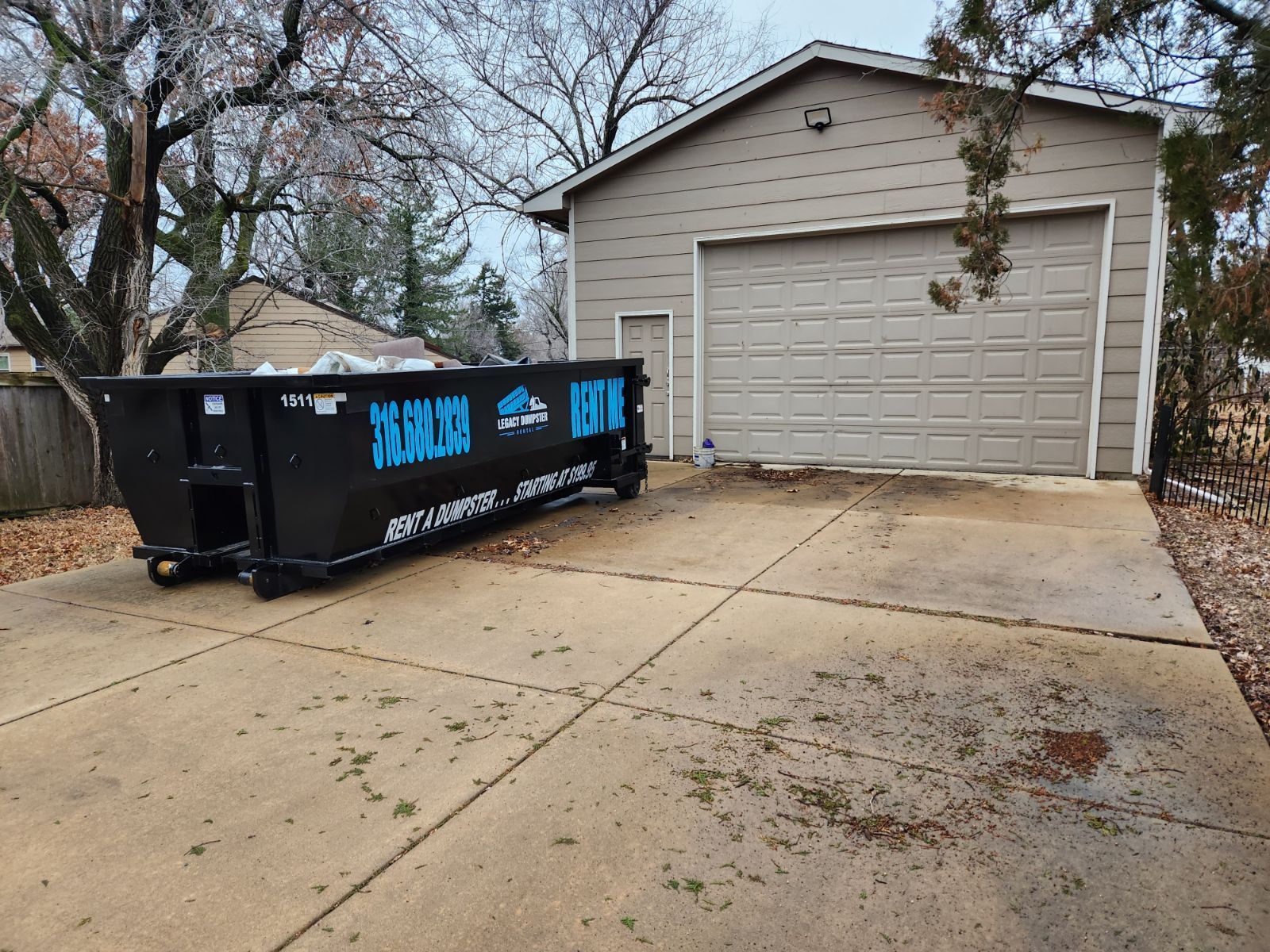 A dumpster is parked in a driveway in front of a garage.