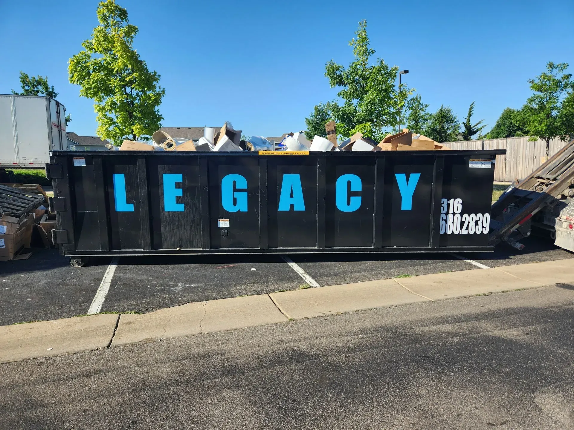 A dump truck is dropping off a 20 yard dumpster in the grass in Haysville