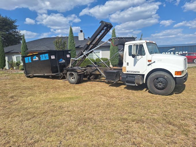 a dump truck is towing a dumpster in a field .