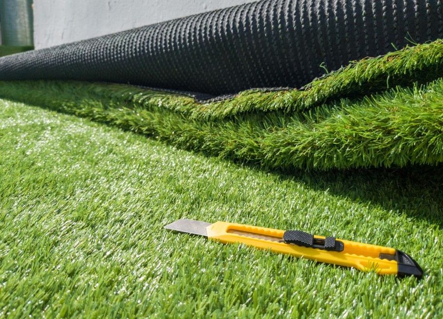 Artificial turf being unrolled, with a utility knife on the grass.