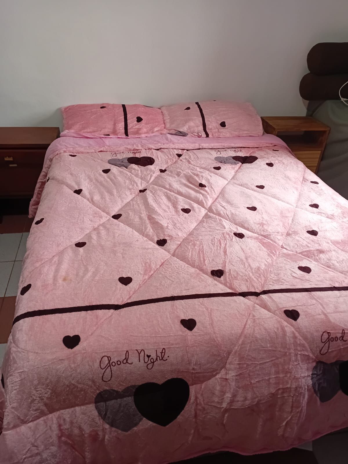 Una cama con un edredón rosa y almohadas encima.