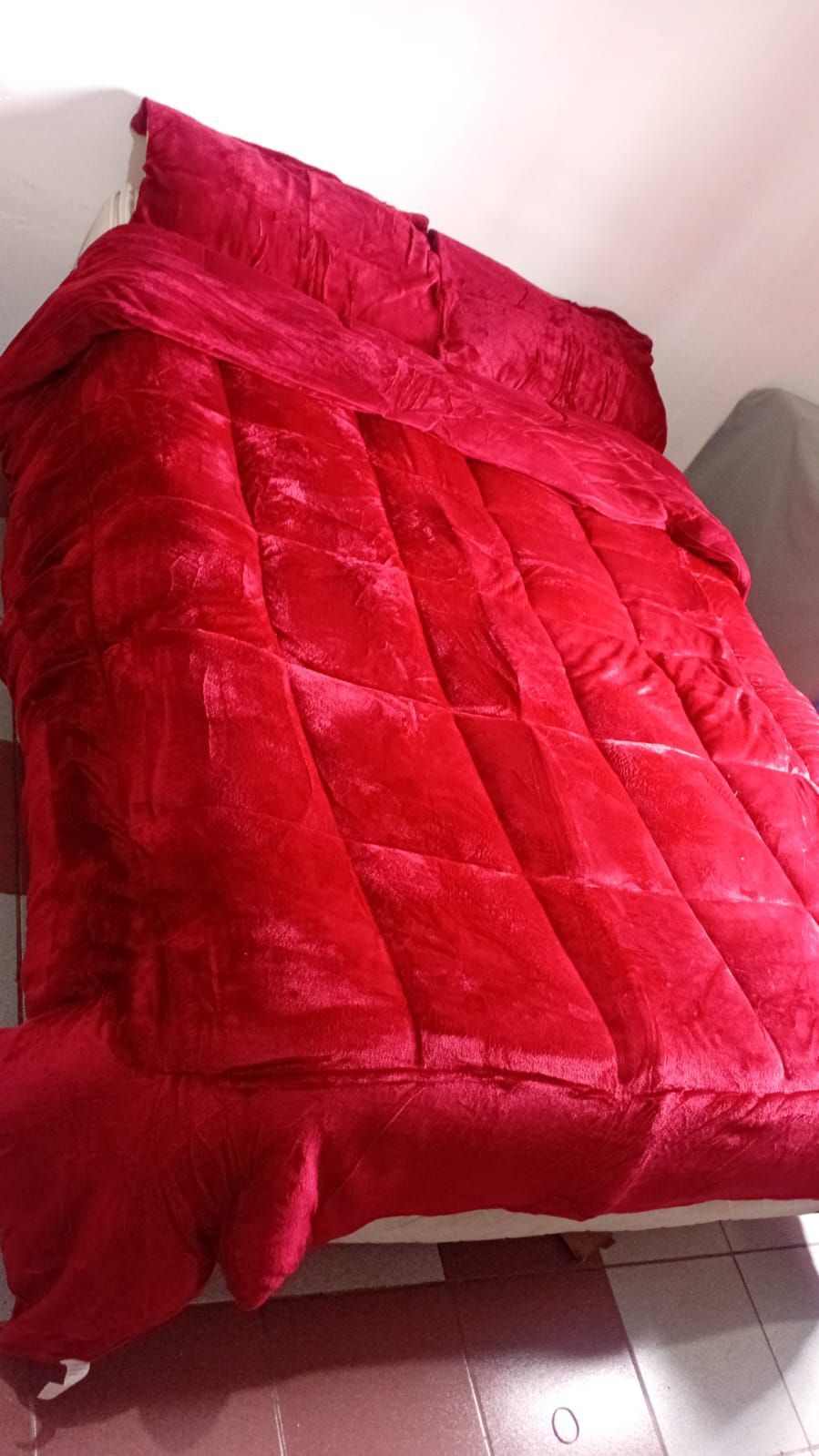 Una cama con un edredón rojo y almohadas encima.