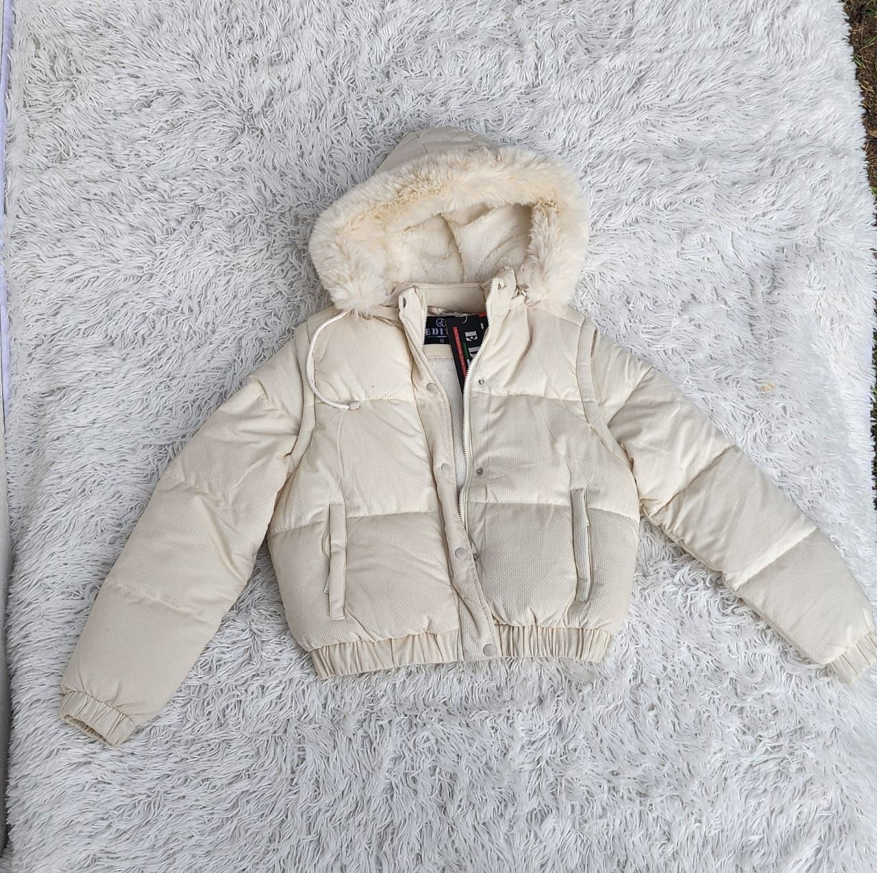 Una chaqueta blanca con capucha de piel yace sobre una manta blanca.