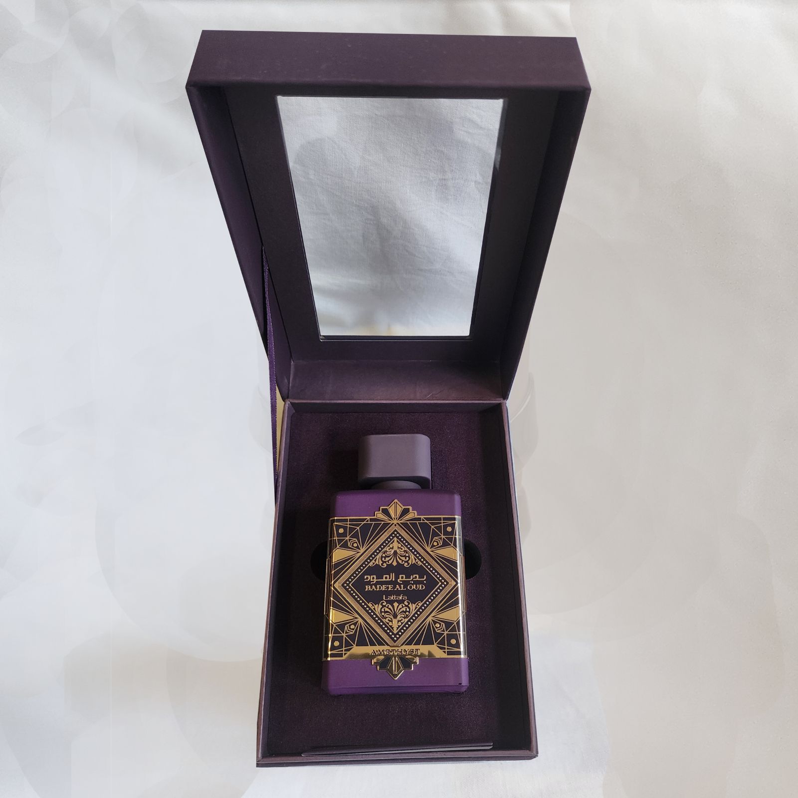 Un frasco de perfume en una caja morada con un espejo.
