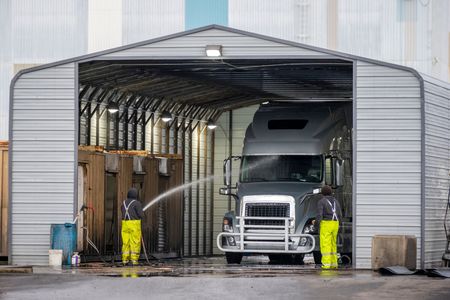 Two workers washing a semi truck inside an industrial truck wash bay