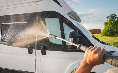 Person pressure-washing a white van outdoors with a hose sprayer