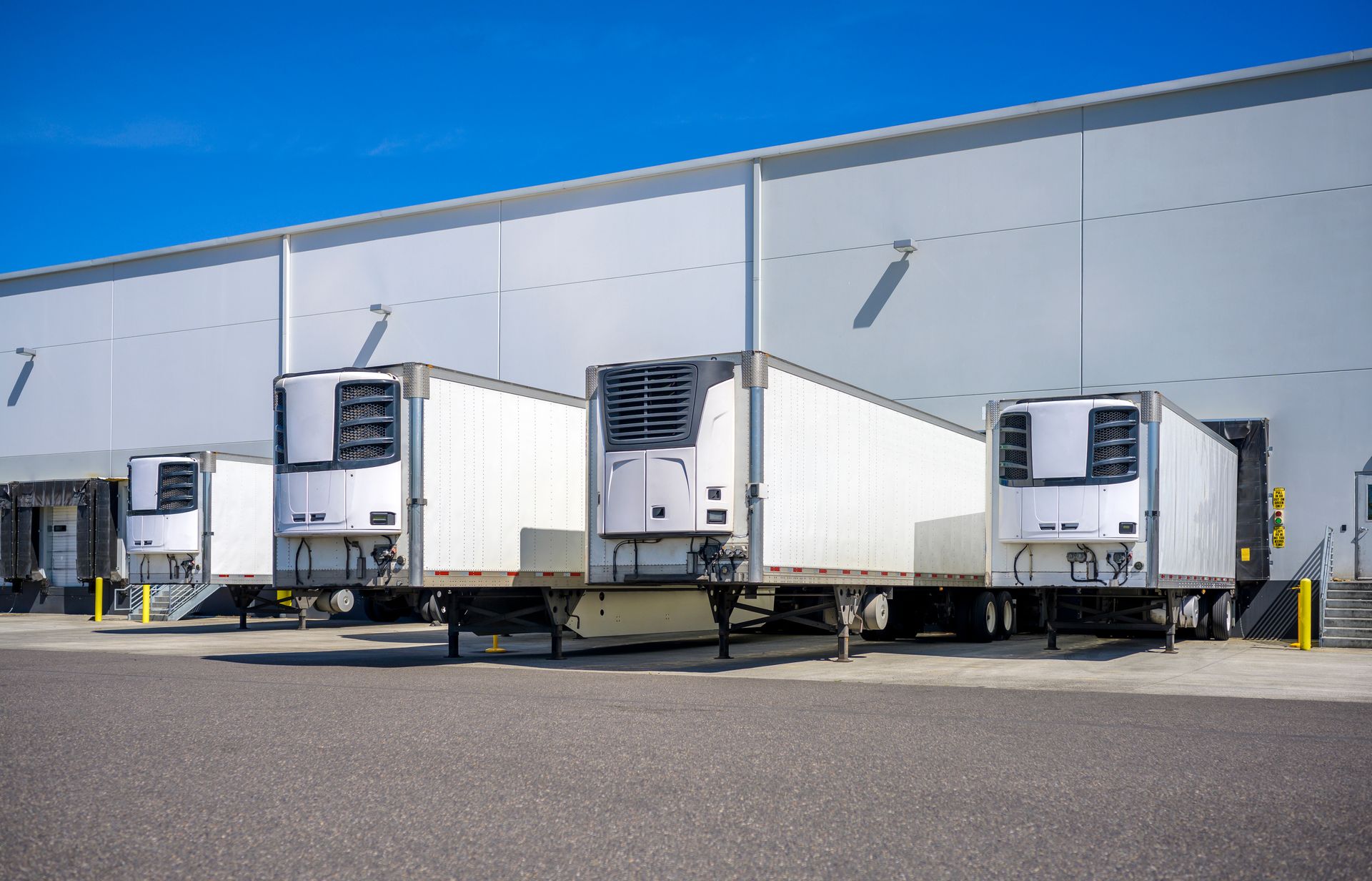 Refrigerated semi-truck trailers docked at a warehouse loading dock, under a blue sky.