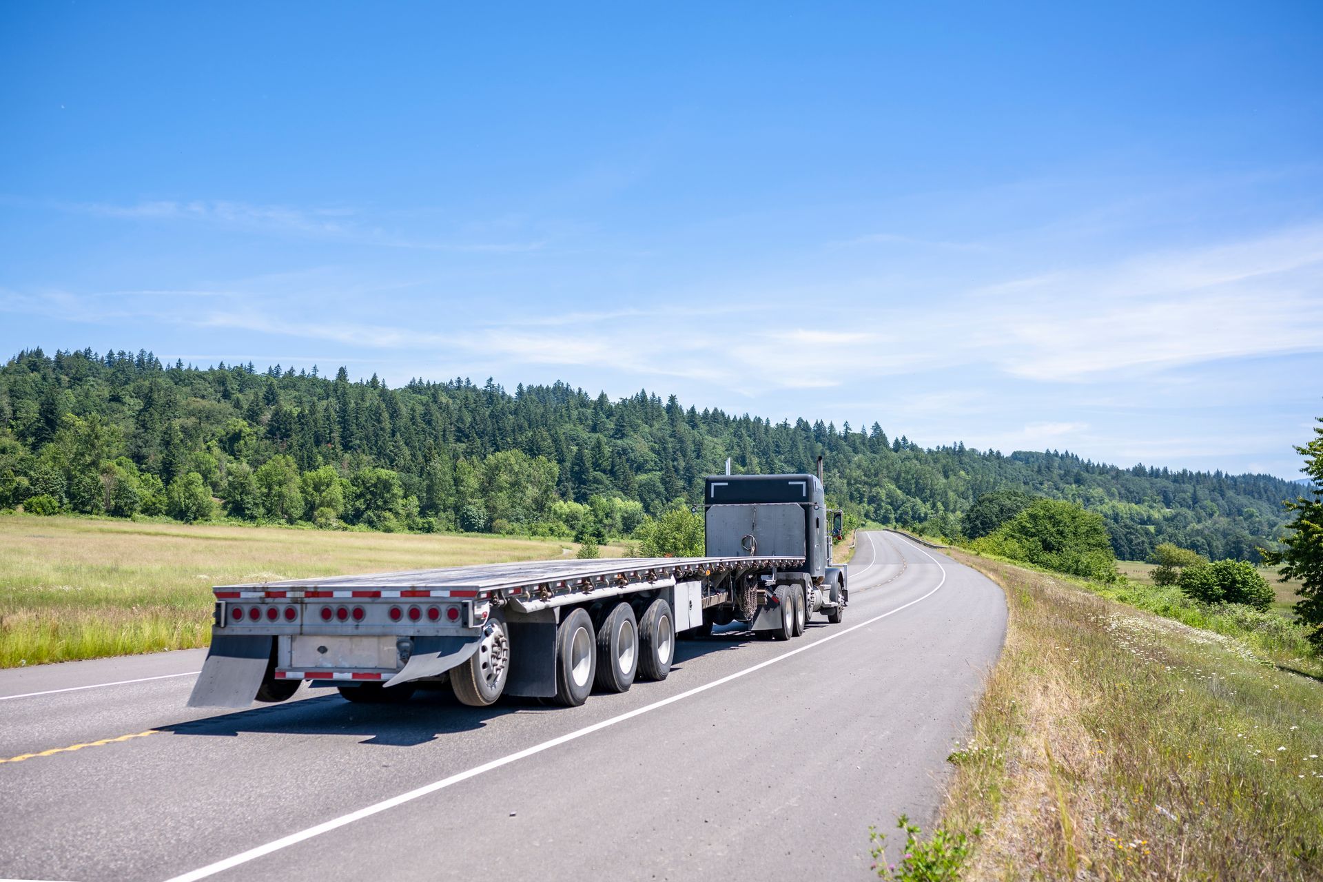 A gold Cadillac is being towed on a trailer by a yellow pickup truck on a roadside.