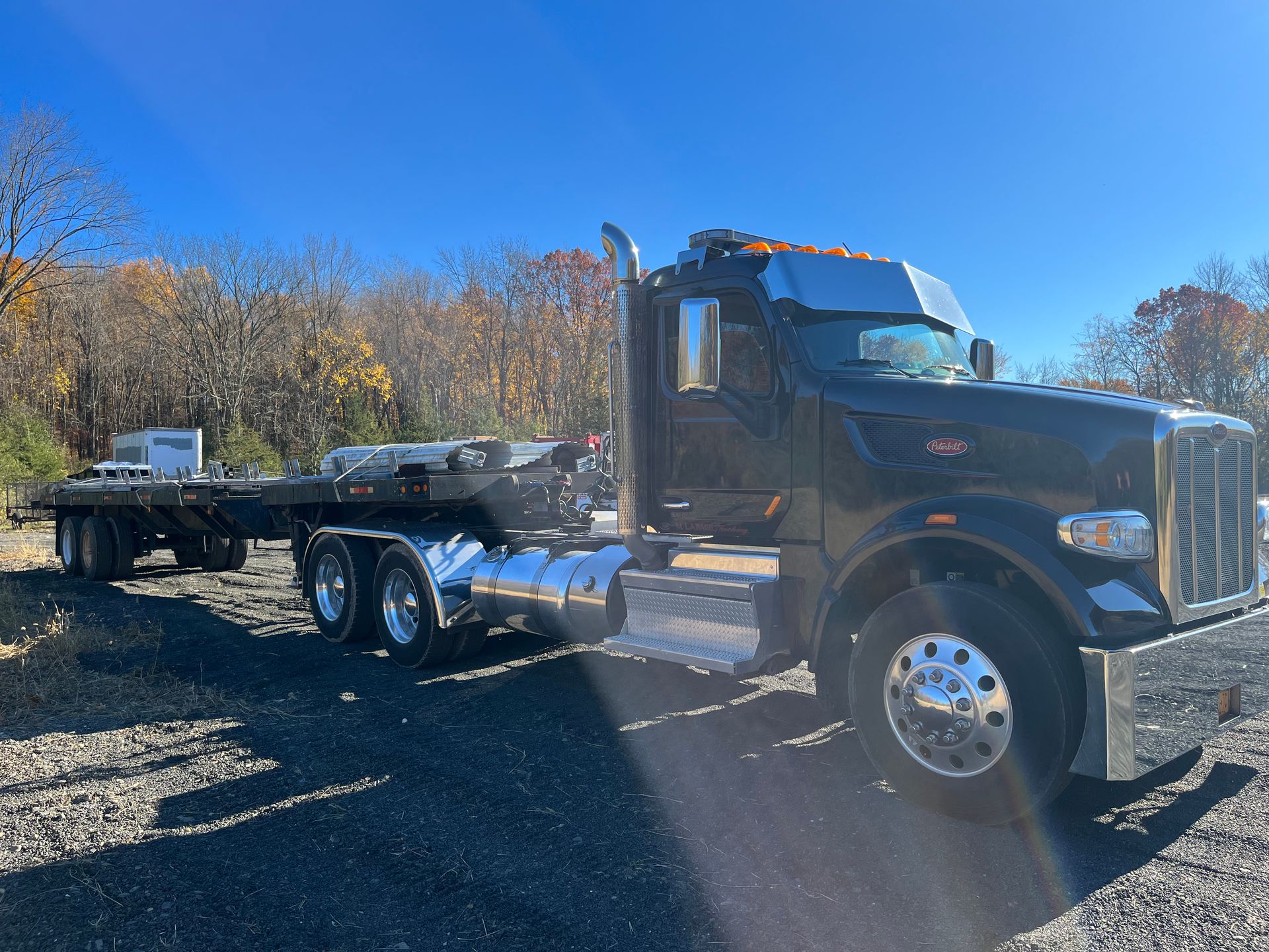 A black semi truck with a flatbed trailer attached to it is parked in a gravel lot.