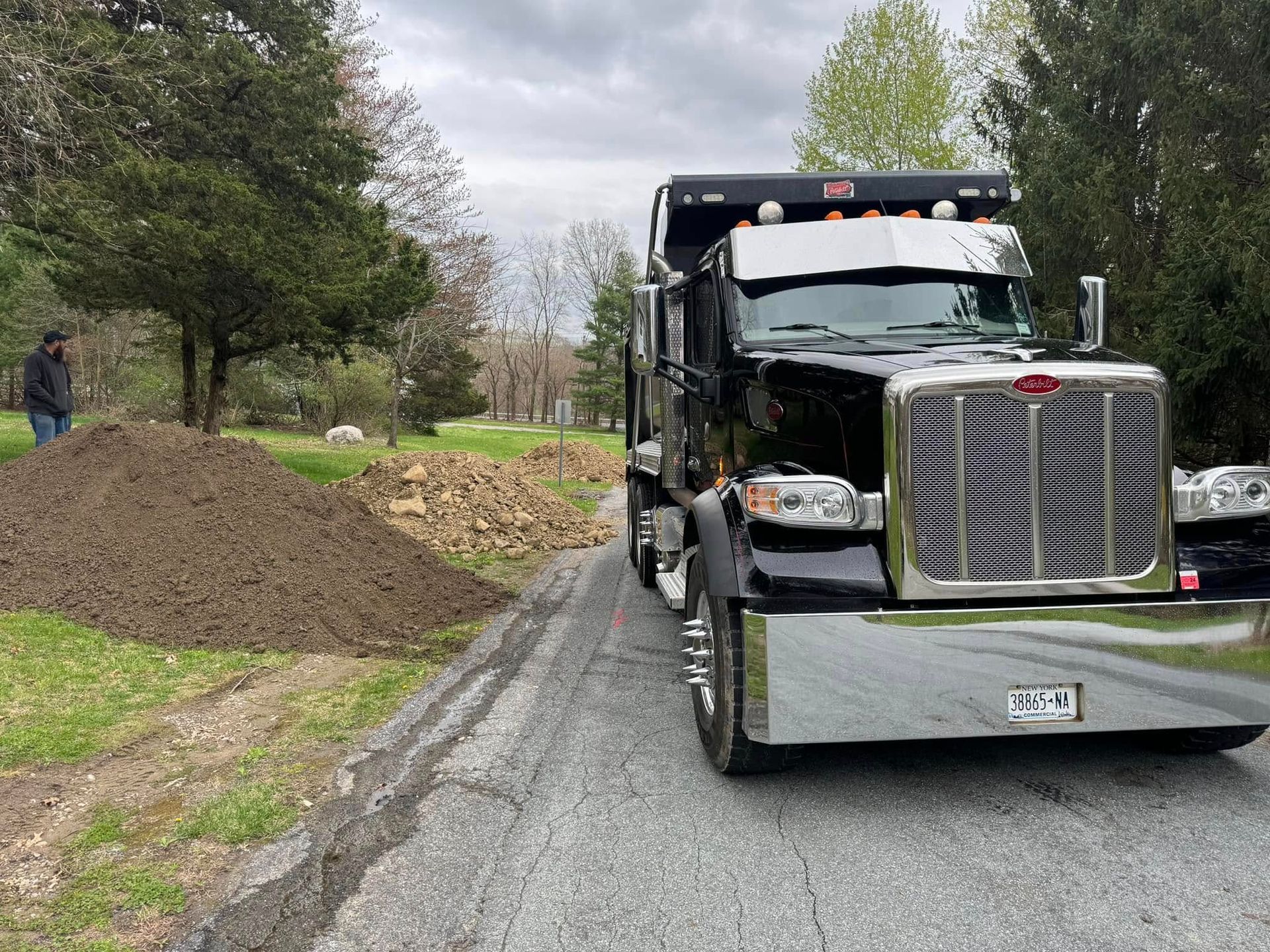 A dump truck is driving down a road next to a pile of dirt.