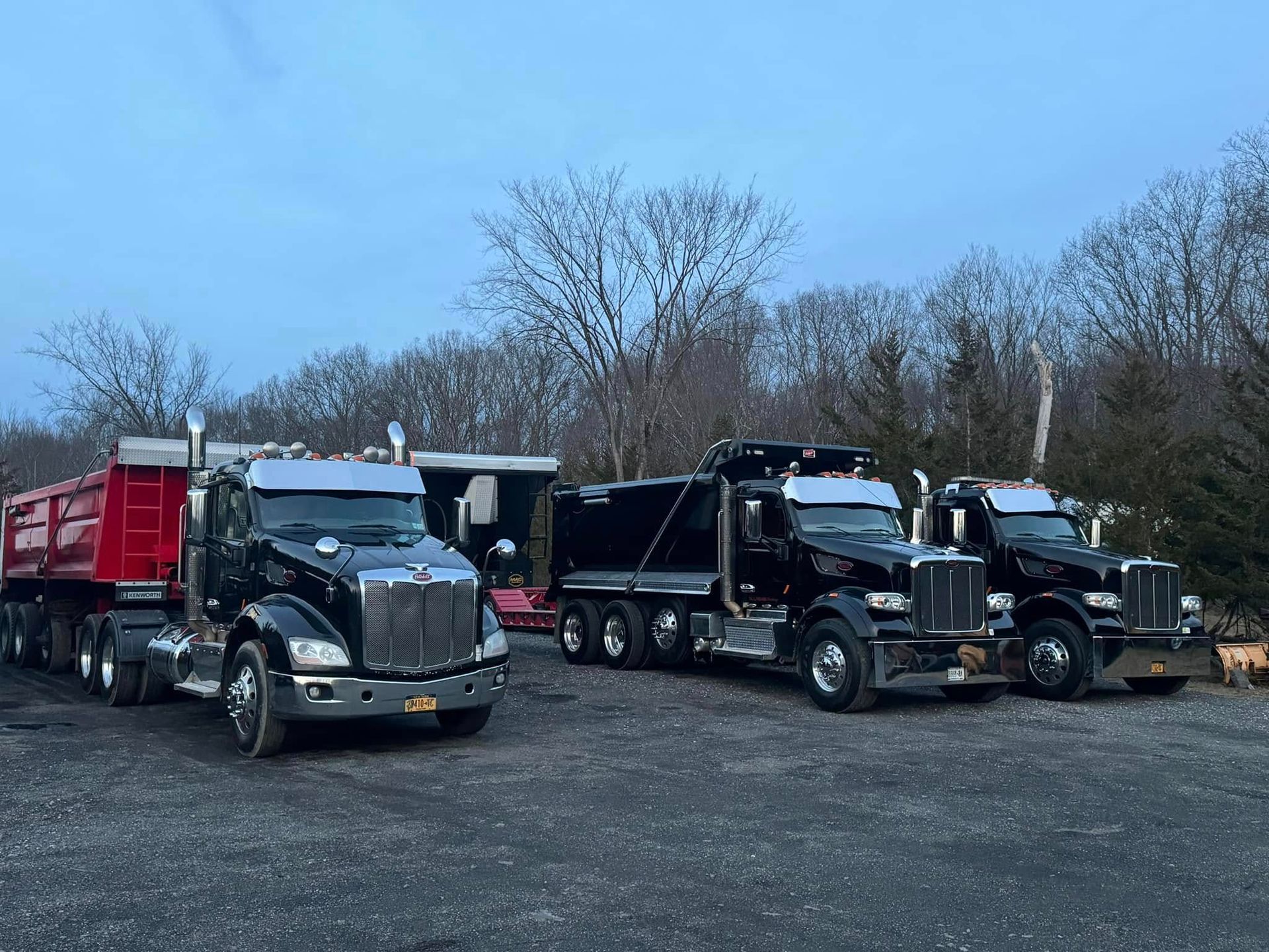 Three dump trucks are parked next to each other in a gravel lot.