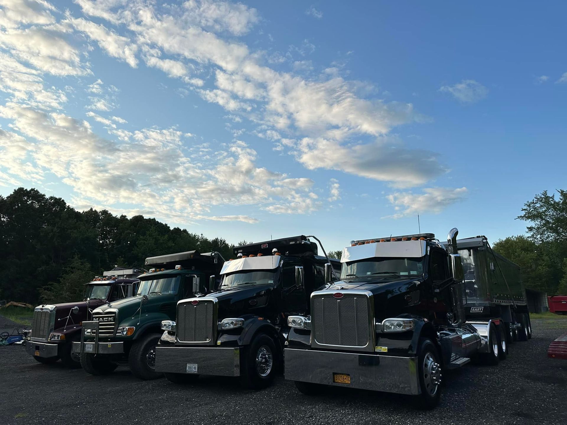 A row of semi trucks are parked in a gravel lot.