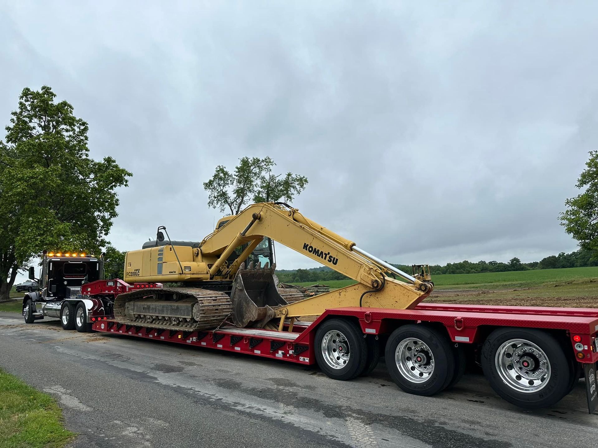 A yellow excavator is being transported on a red trailer.