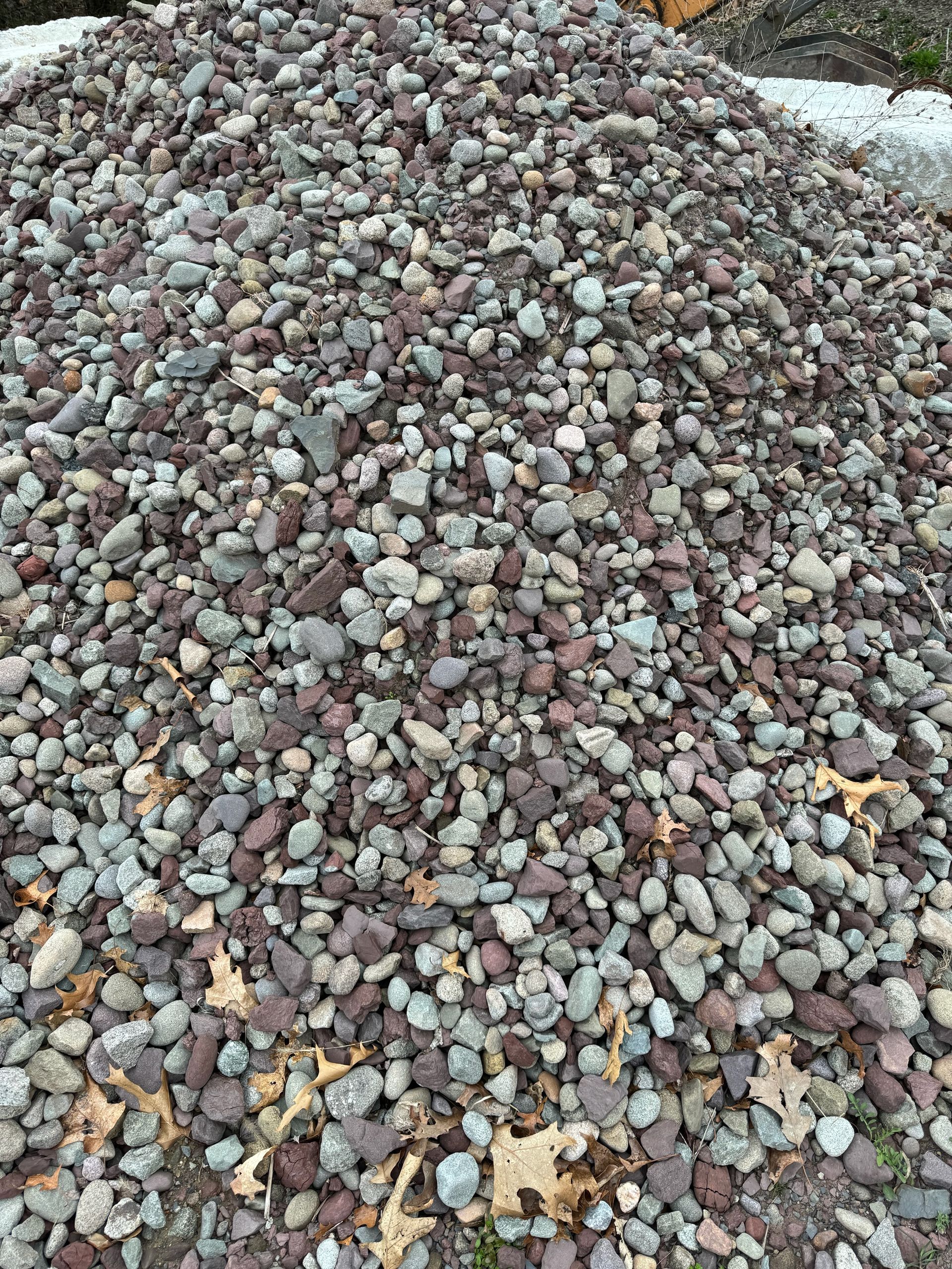 A pile of gravel with leaves on it is sitting on the ground.