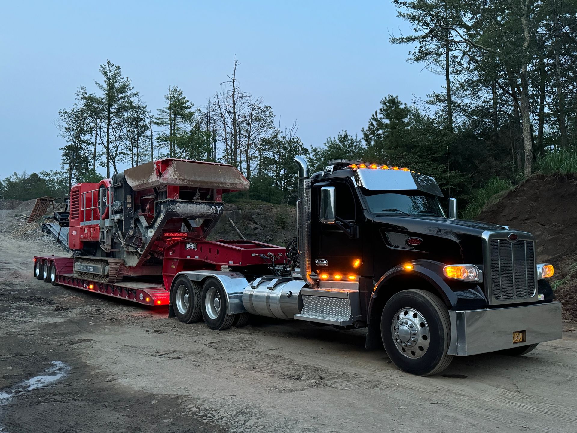 A semi truck is carrying a machine on a trailer on a dirt road.