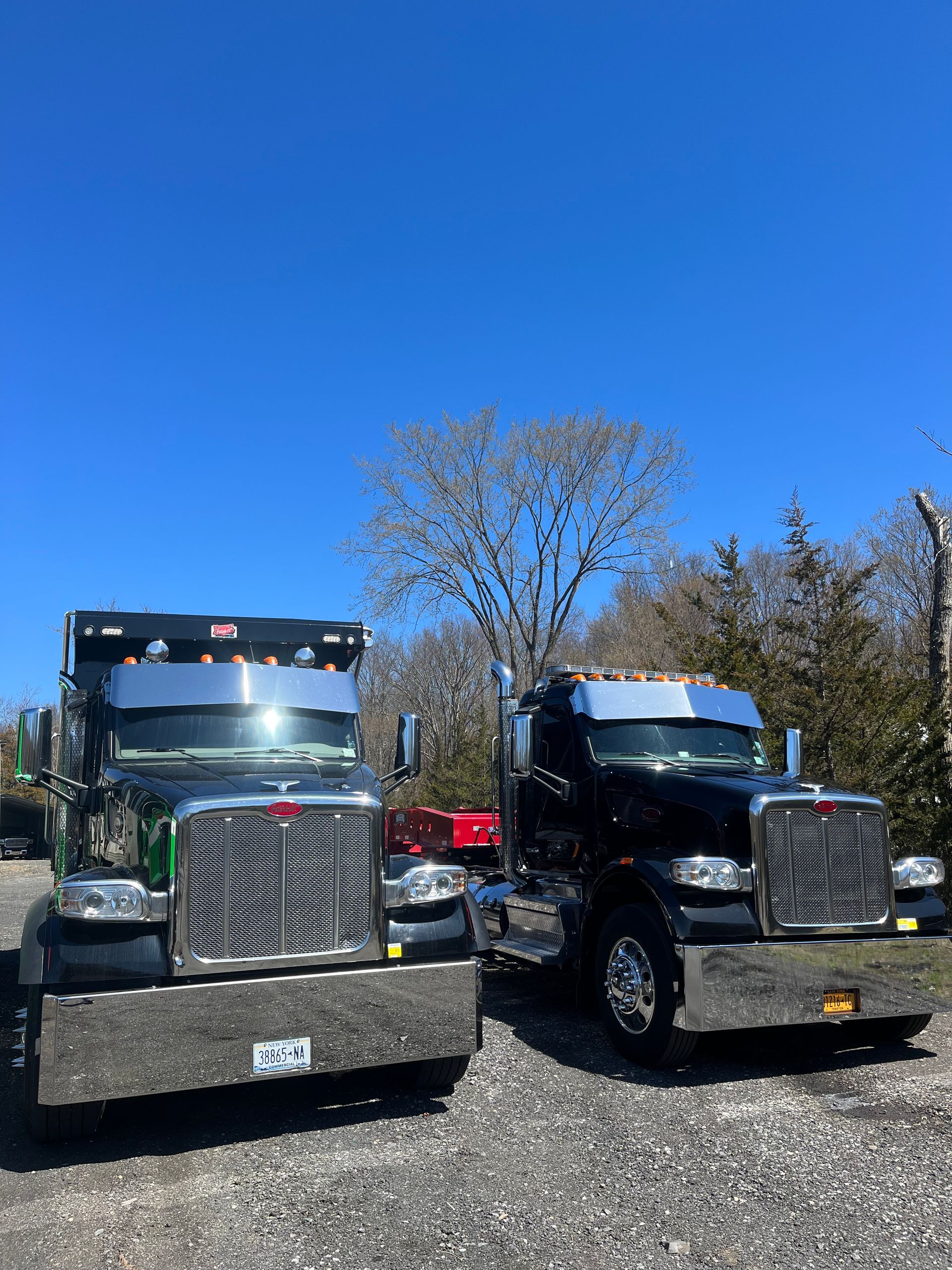 Two semi trucks are parked next to each other on a gravel road.