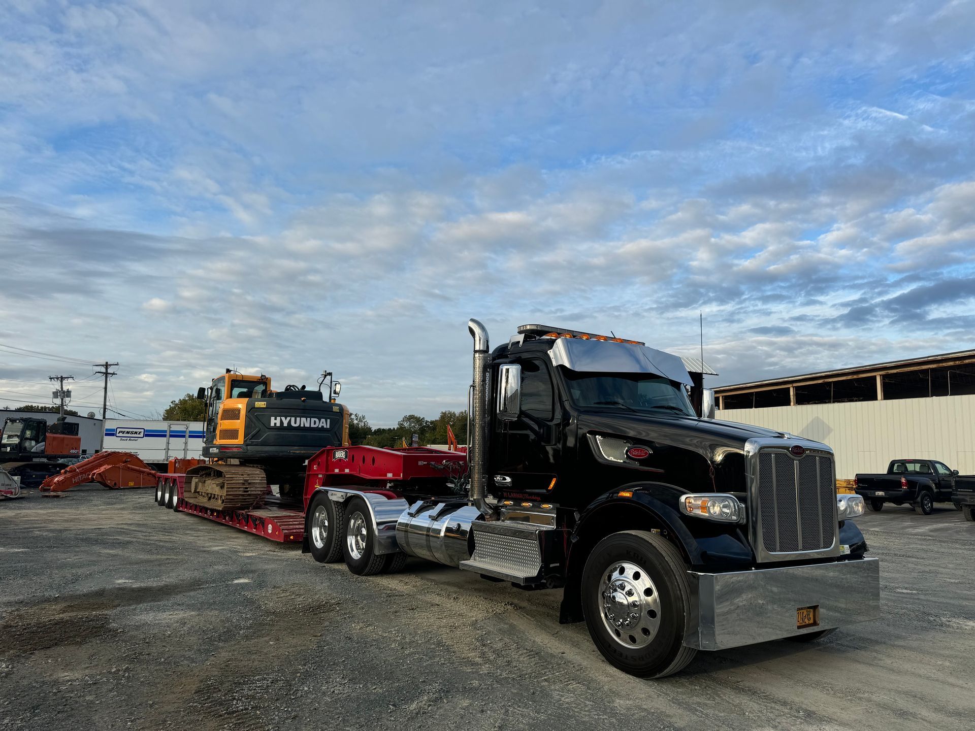 A black semi truck is carrying a yellow excavator on a trailer.